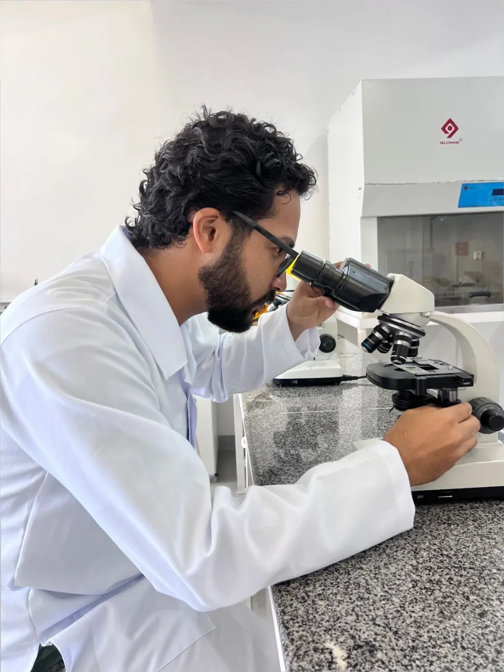 Daniel P Francisco in a lab coat looking through a microscope in a laboratory