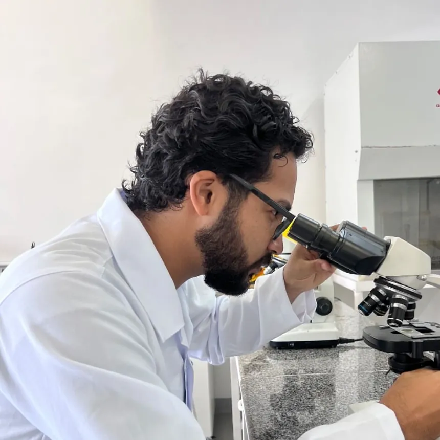 Daniel P Francisco in a lab coat, looking through a microscope in a laboratory